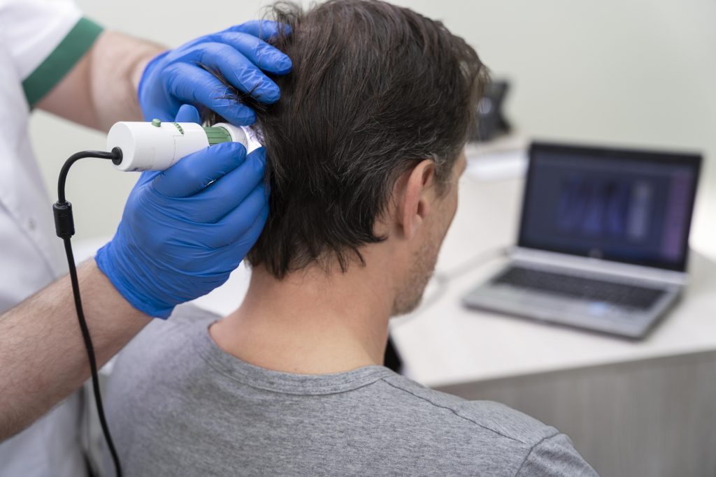 Primer plano de una consulta médica donde se realiza un análisis del cuero cabelludo mediante tricoscopia digital para evaluar la salud folicular.