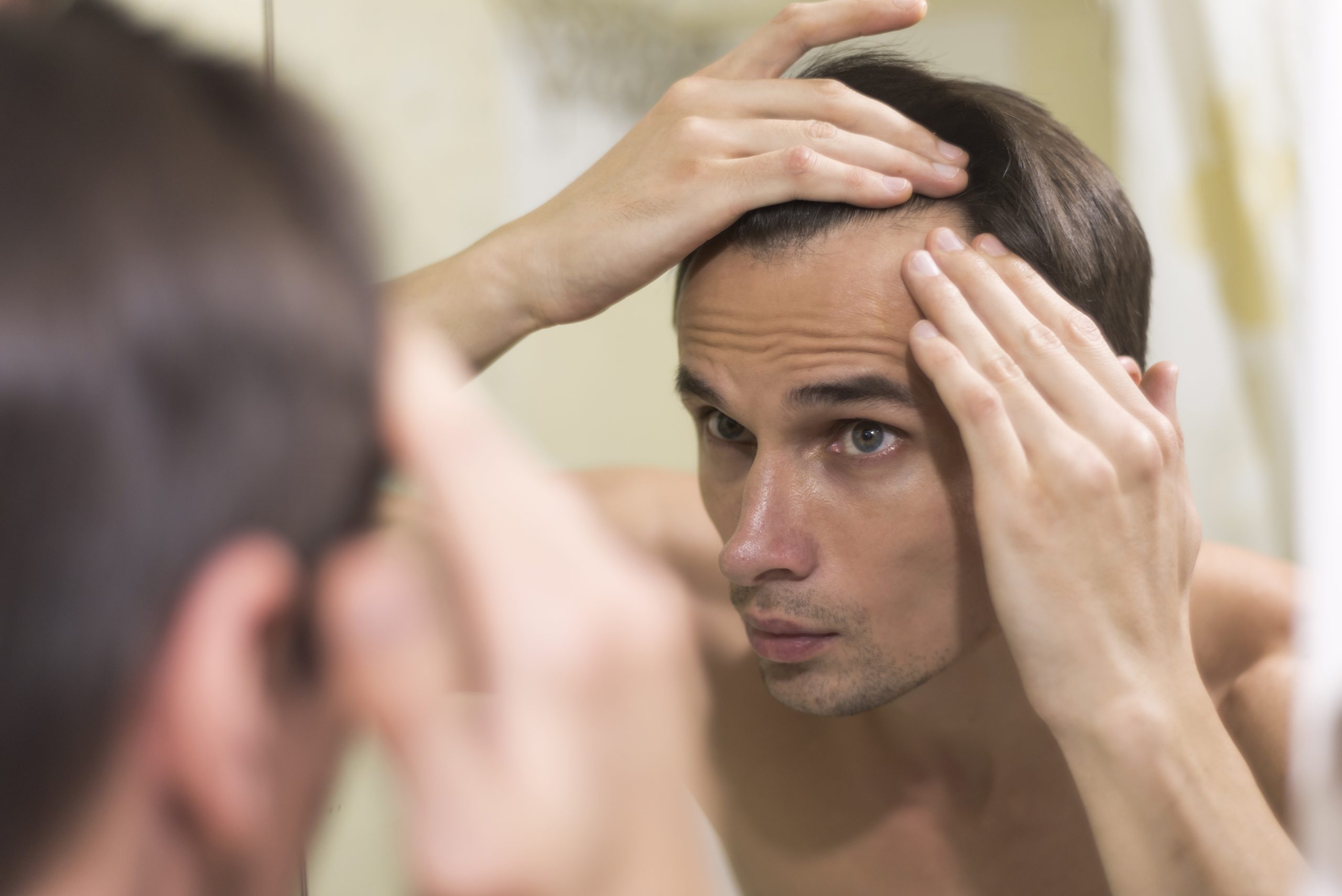 Hombre de mediana edad observando su cabello saludable frente al espejo, reflejando seguridad y bienestar tras un tratamiento capilar.