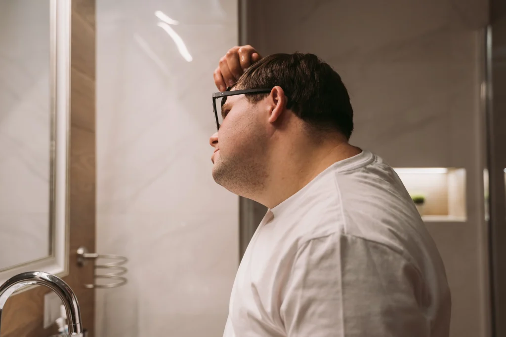 Primer plano de un hombre observando atentamente la densidad de su línea de nacimiento del cabello frente a un espejo, con una actitud de autocuidado.