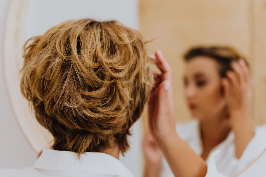 Mujer peinándose y revisando suavemente la raya de su cabello para verificar el volumen y la densidad en la zona central de la cabeza.
